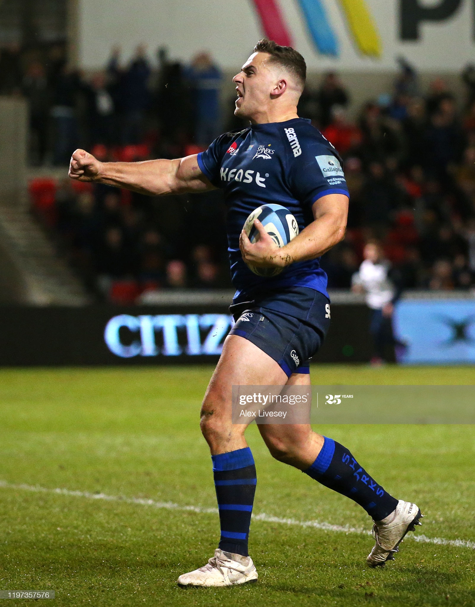 Man in blue shirt and shorts holding a rugby ball punching the air outward in celebration